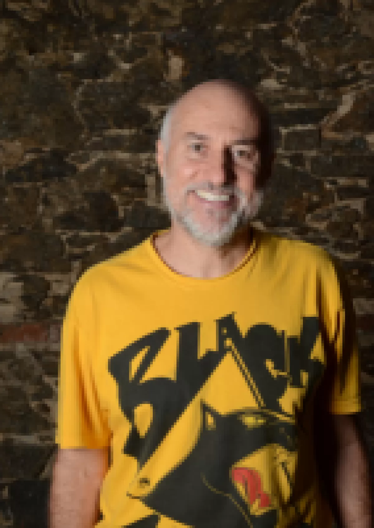 A balding man smiles at the camera in a yellow tshirt.